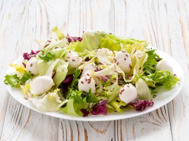 Salata yapraklarını mozzarella ve keten tohumlarıyla karıştırın beyaz tahta arka planda beyaz bir tabakta