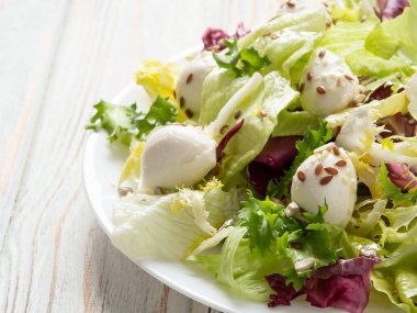 Mozarella soslu taze sebze salatası, marul yaprakları ve keten tohumları, beyaz tabakta.