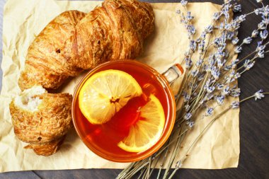 Siyah sıcak çay ve lavanta kokulu bir kağıt arka plan üzerinde taze kruvasanlar ile Kahvaltı