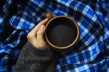 Bir fincan sıcak kahve ekose bir arka plan üzerinde tutan el