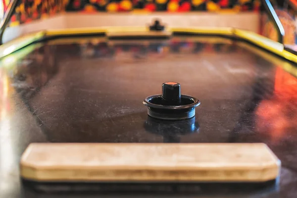 Black Striker on gray Air Hockey Table with Blue Puck and Bokeh Pinball and Games in Background in Arcade.