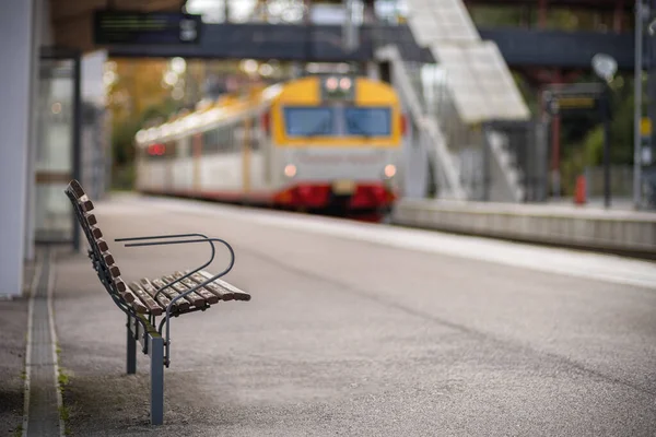 Imagem do banco de madeira na estação de trem com trem embaçado no fundo — Fotografia de Stock