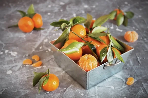 Fresh tangerines with leaves in a steel basket and a peeled Mandarin grey stone