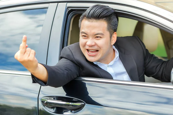 Azjatycka młody człowiek jazdy samochodem i pokazując środkowy palec — Zdjęcie stockowe