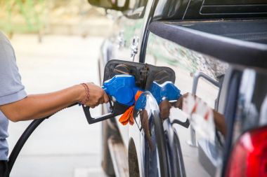 Hand hold fuel nozzle to add fuel in car at filling station. clipart