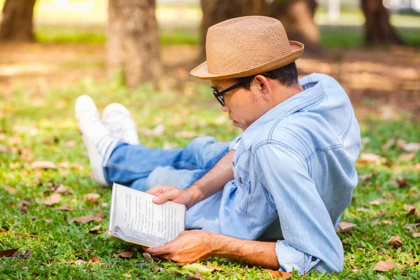 Asiatico giovane uomo leggendo un libro sull'erba nel parco — Foto Stock