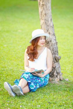 Dizüstü çimlerin üzerine yazma kalemi ile oturan güzel Asyalı kadın