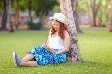 Dizüstü çimlerin üzerine yazma kalemi ile oturan güzel Asyalı kadın