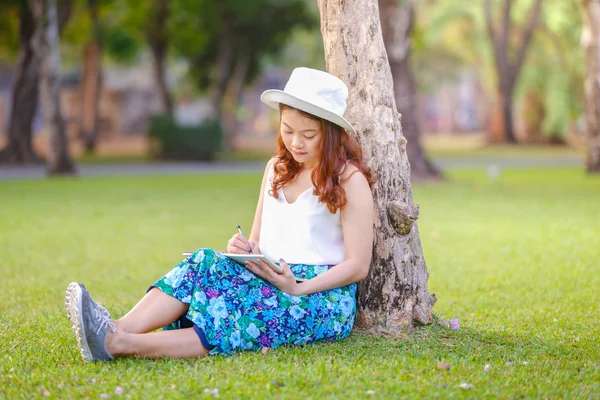 Dizüstü çimlerin üzerine yazma kalemi ile oturan güzel Asyalı kadın