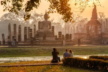 Japanese Man take a photo european traveller in sunrise time at Sukhothai historical park, the old town of Thailand in 800 years ago  clipart