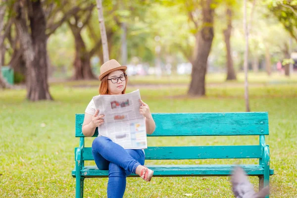 Mulher asiática sentada em um banco de madeira e lendo um jornal em um parque — Fotografia de Stock