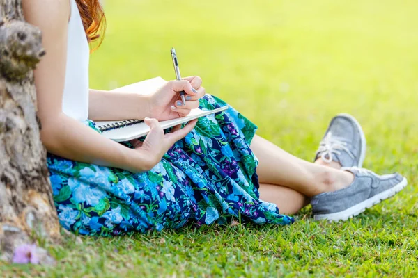 Kobiece ręce z piórem, pisanie na notebooka na trawie poza — Zdjęcie stockowe