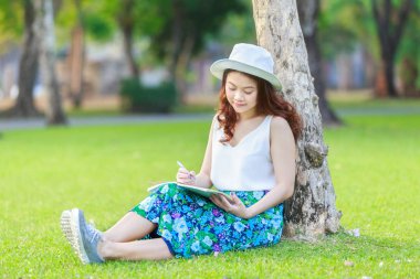Güzel Asyalı kadın kalem yazılı defter ile eller ve çimenlerin üzerinde oturuyordu