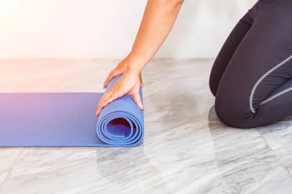 Close-up van aantrekkelijke jonge vrouw vouwen blauwe yoga of fitness mat na uitwerkend thuis in de woonkamer. Gezond leven, keep fit concepten. — Stockfoto