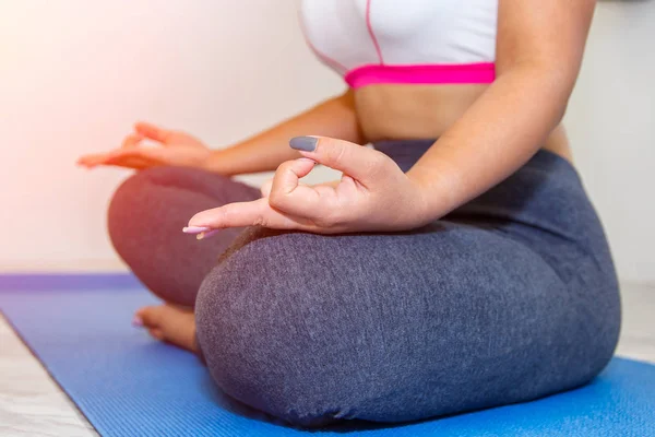 Aantrekkelijke jonge vrouw thuis uit te werken, doen yoga oefening op blauwe mat, zittend in gemakkelijk fatsoenlijk. — Stockfoto