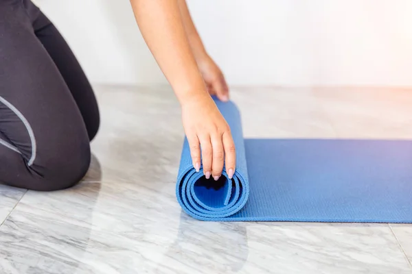 Close-up van aantrekkelijke jonge vrouw vouwen blauwe yoga of fitness mat na uitwerkend thuis in de woonkamer. Gezond leven uw conditie concepten. — Stockfoto