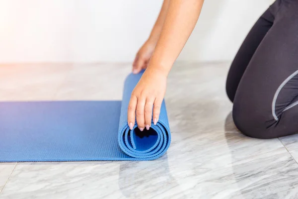 Close-up van aantrekkelijke jonge vrouw vouwen blauwe yoga of fitness mat na uitwerkend thuis in de woonkamer. Gezond leven uw conditie concepten. — Stockfoto