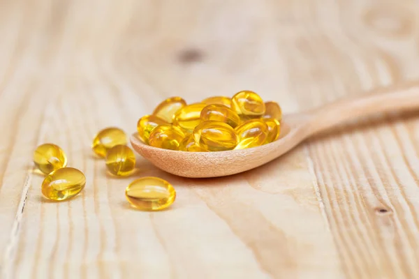 Capsule di olio di pesce con omega 3 e vitamina D su legno di cucchiaio con sfondo in legno, concetto di dieta sana — Foto Stock