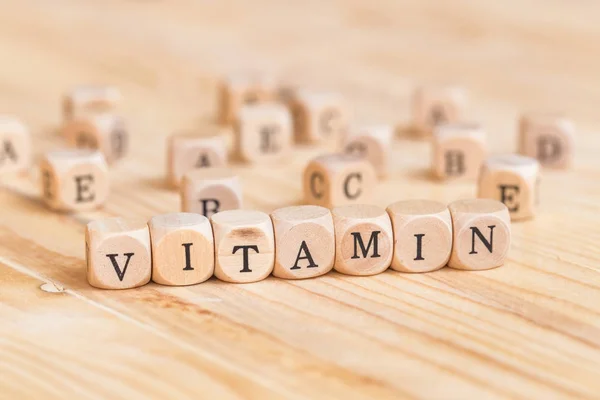 Primo piano parola vitaminica a base di lettere di legno sul tavolo e A B C D E sullo sfondo del tavolo, concetto di salute — Foto Stock
