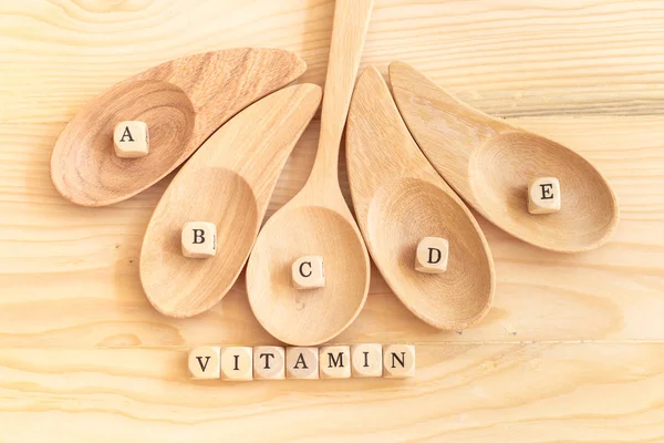 Vista dall'alto vitamina parola fatta da lettere di legno sul tavolo e A B C D E sul cucchiaio di legno, concetto di salute — Foto Stock