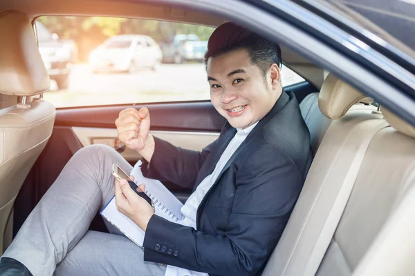 Hombre de negocios guapo contento de tener éxito sentado en el asiento trasero del coche y el teléfono conmovedor — Foto de Stock