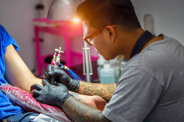 Close up tatuagem artista demonstra o processo de obter tatuagem preta com tinta. Mestre trabalha em luvas estéreis pretas . — Fotografia de Stock