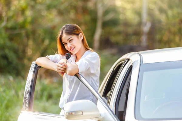 Mujer asiática feliz conductor mostrando las llaves del coche y apoyado en la puerta del coche . — Foto de Stock