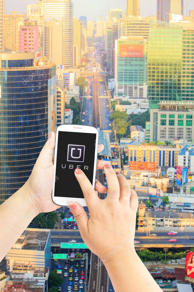 BANGKOK, THAILAND - JUNE 5,2015 : A woman hand holding Uber app showing on smartphone on Sathon business building in sunset or time out background, Uber is smartphone app-based transportation network.