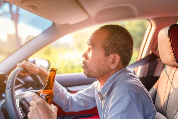 酔ってアジアの若者は日没の背景を持つビールのボトルで車を運転し、危険な運転の概念 — ストック写真