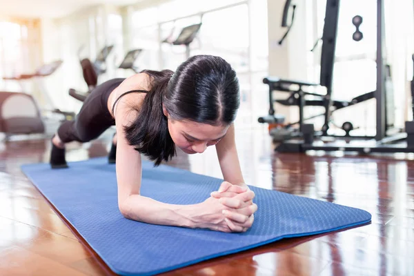 Mooie jonge aziatische vrouw uit te werken in de sportschool en doen yoga oefening op blauwe mat. — Stockfoto