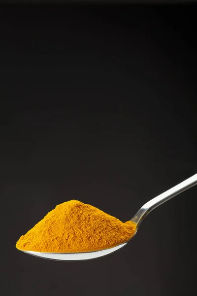 Spoon of ground turmeric on black background — Stock Photo, Image