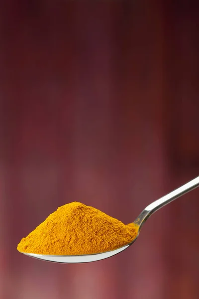 Spoon of ground turmeric on maroon background — Stock Photo, Image