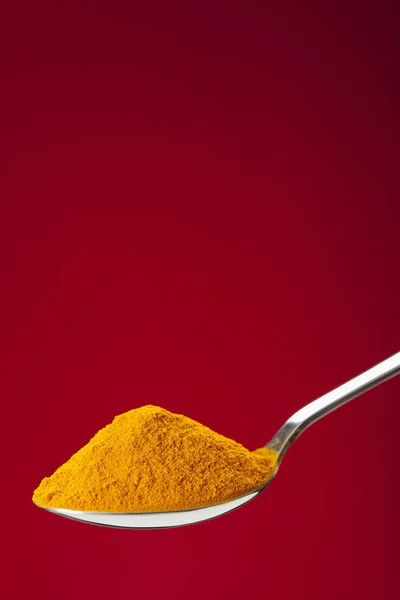 Spoon of ground turmeric on red background — Stock Photo, Image