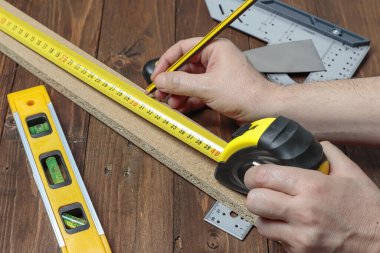 Diğer DIY araçları ile bir set üzerinde bir ahşap şerit uzunluğunu ölçmek için bir kalem ve bir esnek ölçer kullanarak üst iki elin yatay görünümü