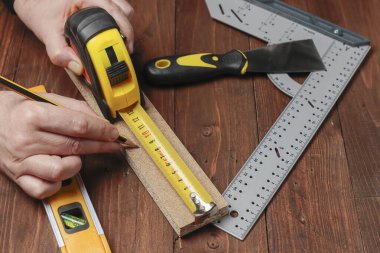 Diğer DIY araçları ile bir set üzerinde bir ahşap şerit uzunluğunu ölçmek için bir kalem ve bir esnek ölçer kullanarak üst iki elin yatay görünümü