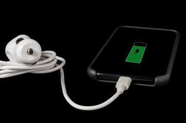 Siyah arkaplanda izole edilmiş beyaz renkli bir araba çakmağına bağlı şarj edilmiş bir cep telefonunun yatay görünümü