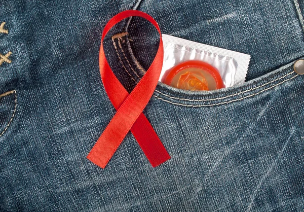Червоний презерватив у блакитній кишені джинсів та інформованість СНІДу червона стрічка — стокове фото