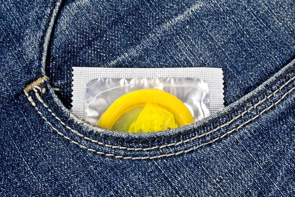 Preservativo amarelo em um bolso de calça azul — Fotografia de Stock