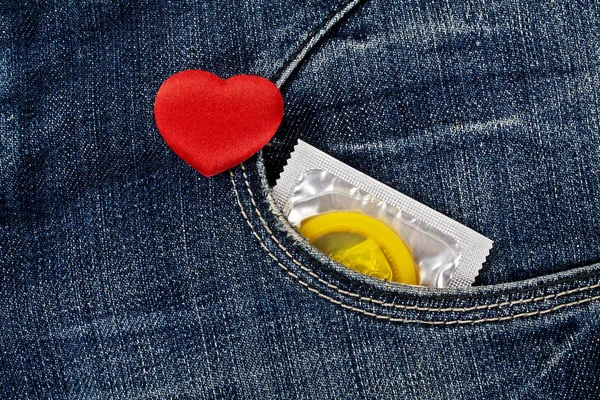 Coração vermelho e preservativo amarelo no bolso azul jeans — Fotografia de Stock