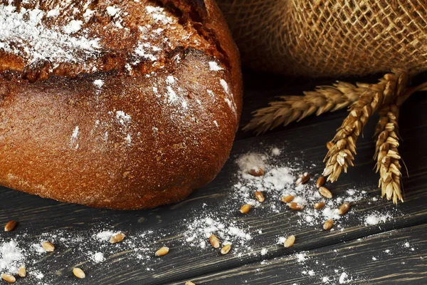 Frisch gebackenes traditionelles Brot und Weizen auf Holztisch — Stockfoto