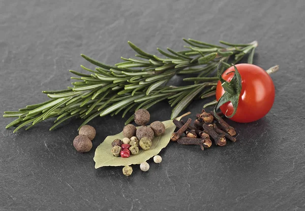 Rosemary, laurel leaf, pepper, cloves and cherry tomatoes on bla