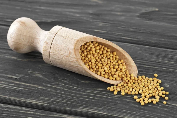 Yellow mustard seeds in wooden scoop on wood background — Stock Photo, Image