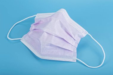 Mavi arka planda mor tıbbi maske. Lastik kulaklıklı cerrahi maske..
