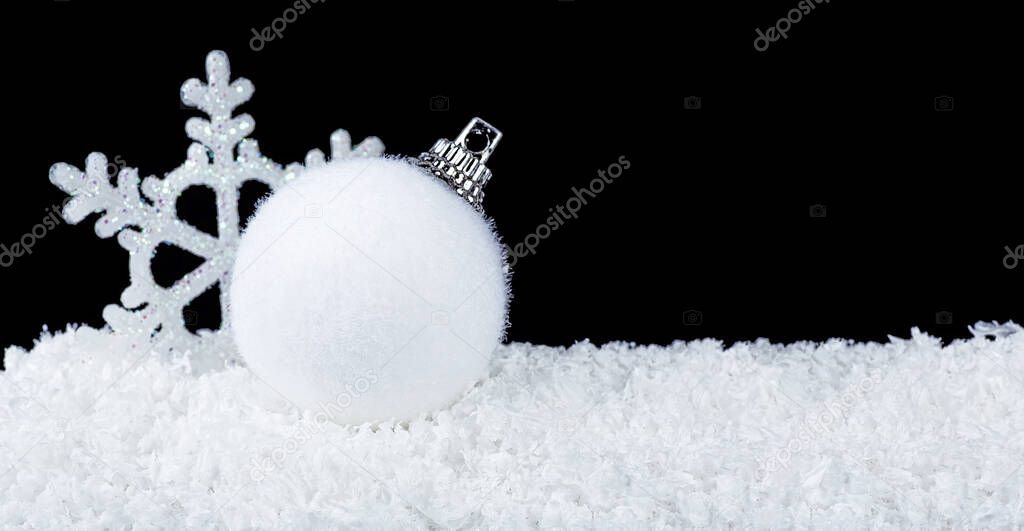 White decorative snowflake and christmas ball on white snow on a black background