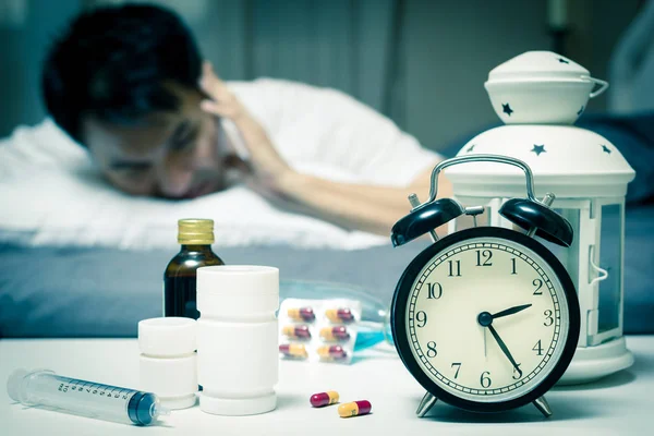 Asian man in bed with tablets and drugs suffering insomnia, hangover, headache at night Stock Image