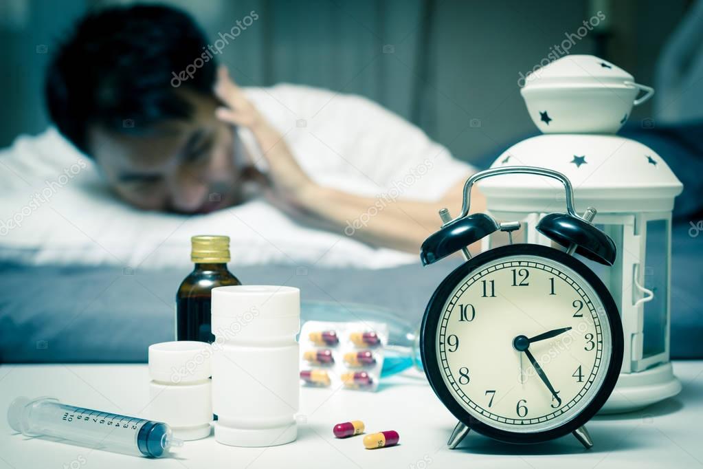 asian man in bed with tablets and drugs suffering insomnia, hangover, headache at night