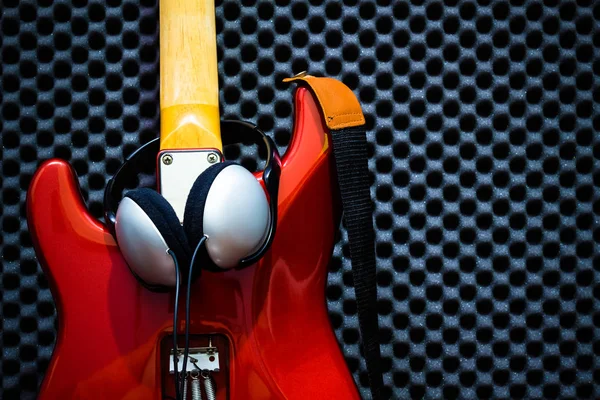 Casque à l'arrière de la guitare électrique rouge, fond de tableau acoustique — Photo