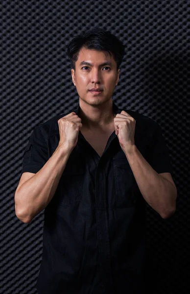 Asiático guapo hombre en negro camisa posando en negro studio difusión tablero — Foto de Stock