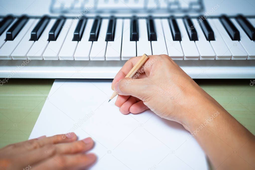 professional composer hands writing songs on blank white paper with studio keyboard & computer