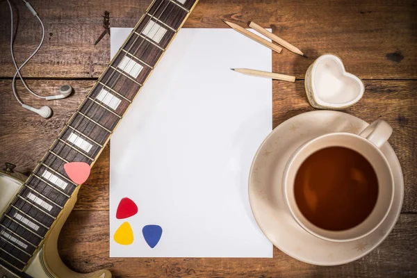 Guitare électrique, papier blanc vierge et une tasse de thé sur une table en bois — Photo